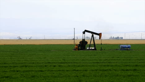 time lapse of an oil well pumping in the middle of a crop field