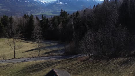 Drone-fly-above-small-hut-in-the-mountains-with-aerial-view-over-cityscape-and-snowy-mountains-in-Austria