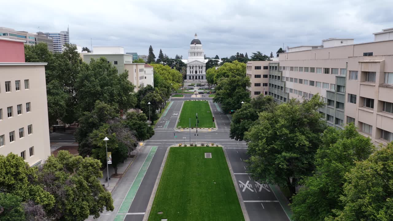 Aerial establishing shot of Sacramento, California, showing State Capitol building, tree lined boulevard, government offices and dramatic cloudy skies in downtown USA. Panorama approaching shot