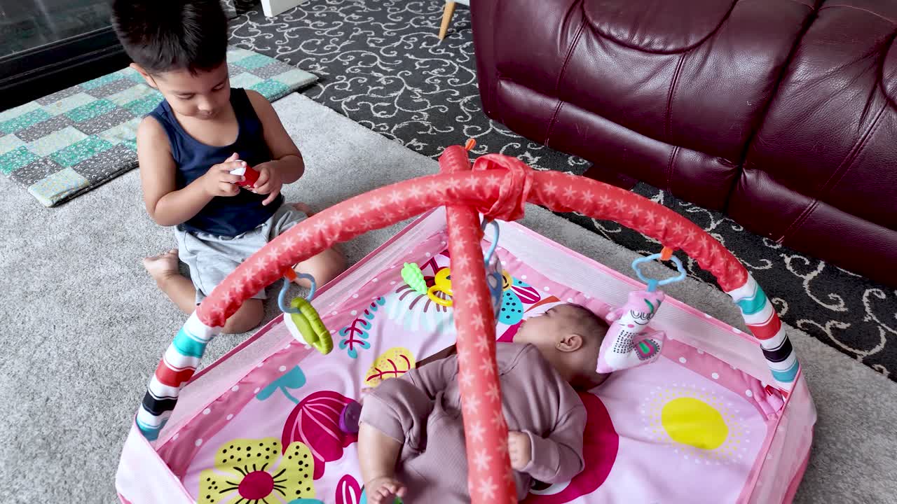 Brother and baby sister playing together at home on a colorful playmat