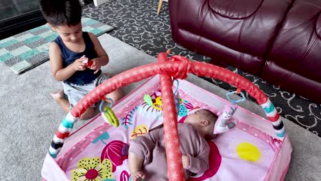 brother and baby sister playing together at home on a colorful playmat