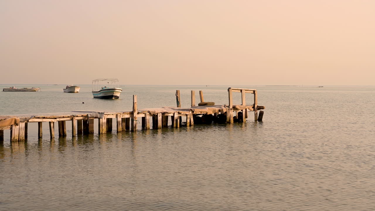 viejo muelle de madera en el agua tranquila del mar sobre el cielo al atardecer con barcos en el fondo, bahrein