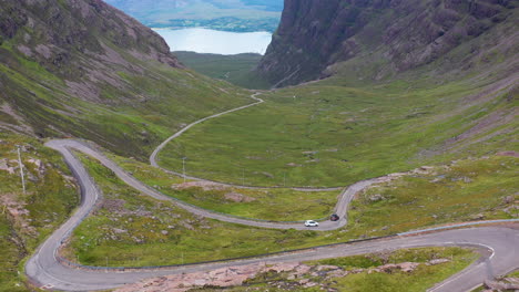 revealing drone shot two vehicles on bealach na ba applecross road through the mountains of the applecross peninsula, in wester ross in the scottish highlands