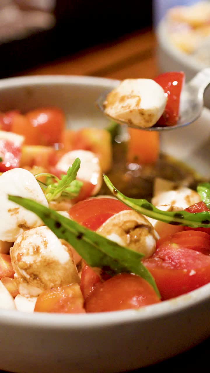Un cucchiaio di metallo raccoglie mozzarella fresca e pomodori da una ciotola con glassa balsamica