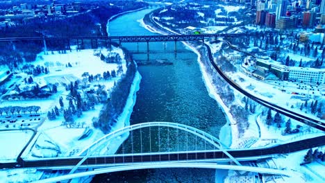 4k winter aerial hold birds view over the walter dale bridge as ice pieces flow down north saskatchewan river, with the vintage old high level bridge in the horizon, while snow covers both parks1-3