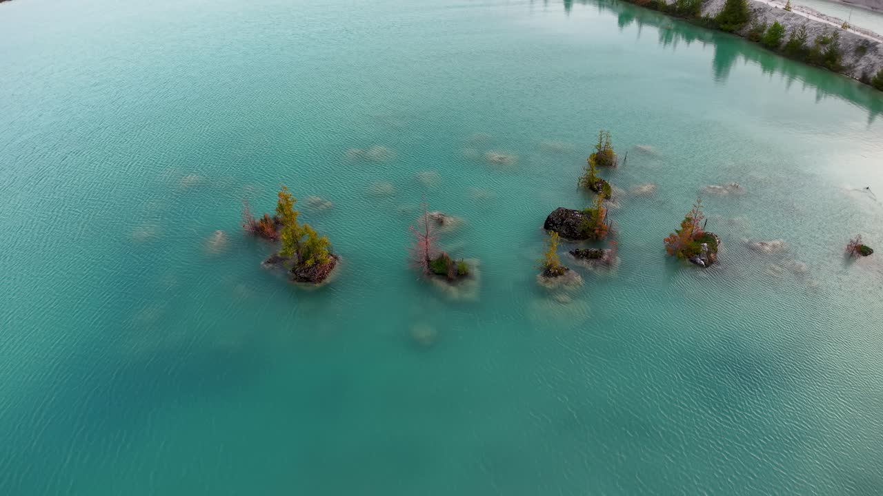 Aerial drone footage of small tree-covered islets scattered across turquoise blue water in a quarry lake