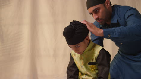 Foto-De-Estudio-De-Un-Padre-Atando-Un-Turbante-En-La-Cabeza-De-Su-Hijo-Sikh-Que-Lleva-Un-Chaleco-Tradicional,-Como-Se-Muestra-En-La-Secuencia,-Parte-9-De-10