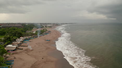 People-relaxing-on-a-tropical-sand-beach-before-the-storm-in-Canggu,-Bali.-Aerial-dolly-view-of-colorful-boats--and-tourists-on-famous-tourist-beach-in-Indonesia