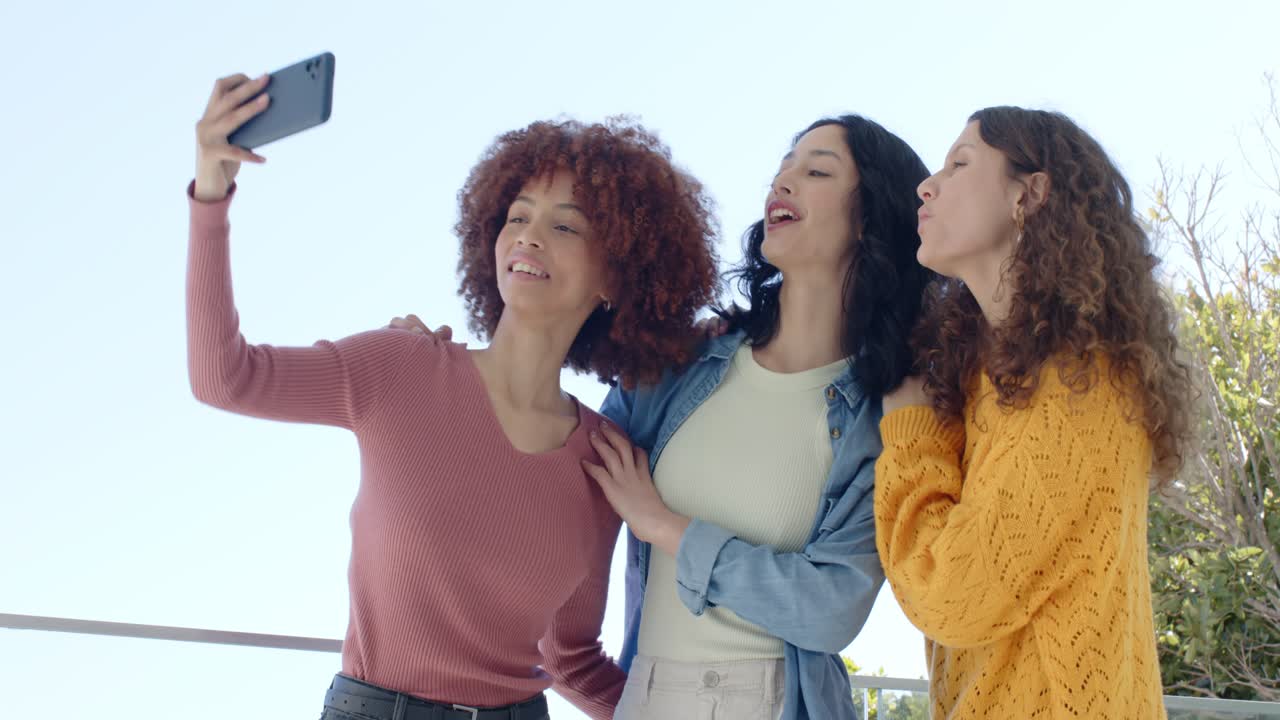 Amiche di etnie diverse che fanno un selfie sul balcone e controllano lo smartphone