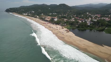 Ocean-waves-crash-on-sandy-golden-shores-of-San-Pancho-Mexico,-aerial-overview