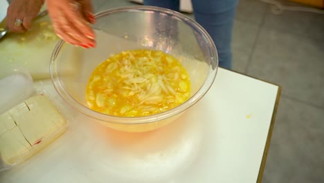 Woman's-Hands-Add-Shredded-Cheese-Into-A-Bowl-With-Beaten-Eggs-And-Mix---close-up,-high-angle