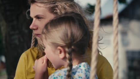 un acercamiento de mamá con la niña balanceándose y hablando juntos en un día de verano.