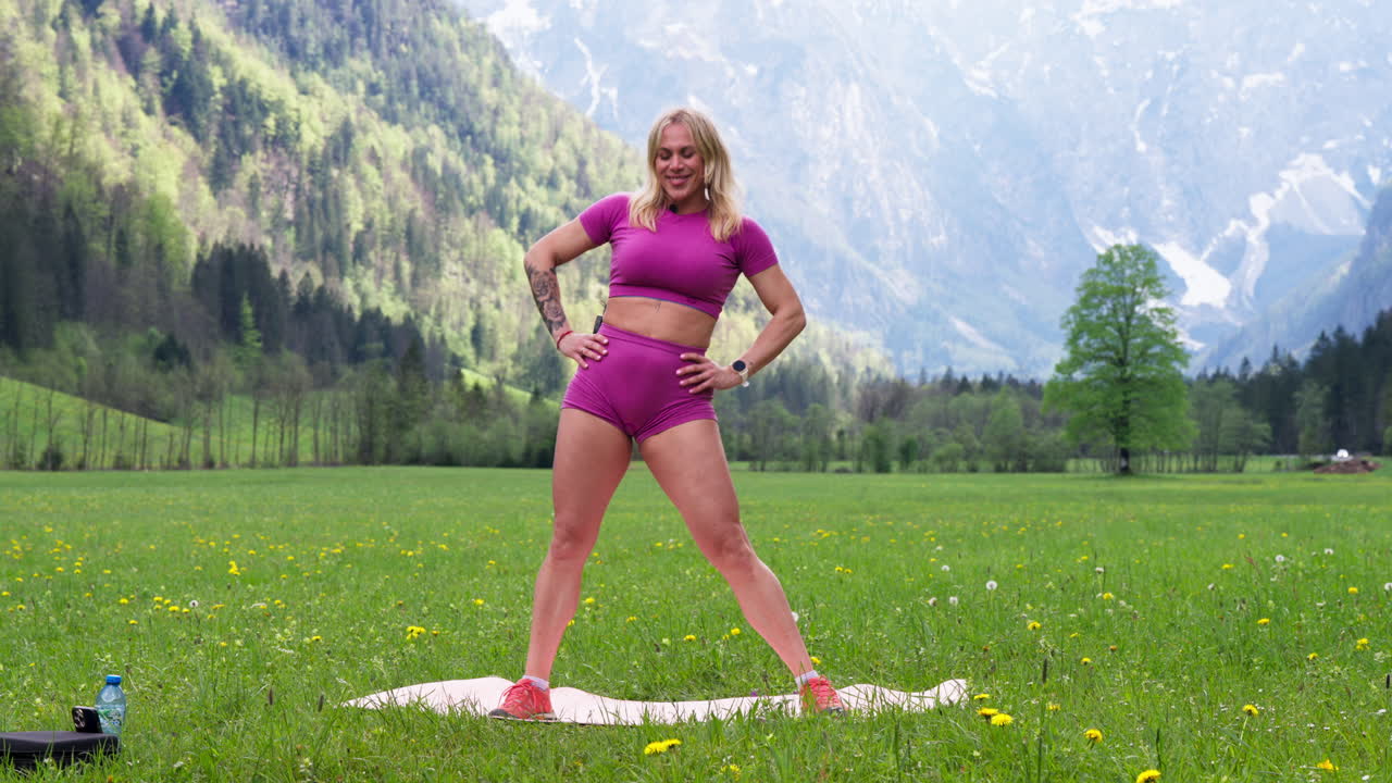 Medium shot of blond woman doing streching with her hips in a green field in the nature, static shot