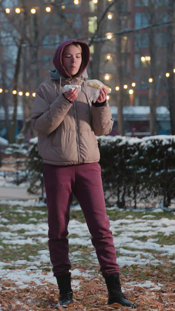 белая леди с закуской, использующая салфетку для очистки рта в зимнем парке с людьми, идущими на размытом фоне, светофоры боке, холодная наружная обстановка