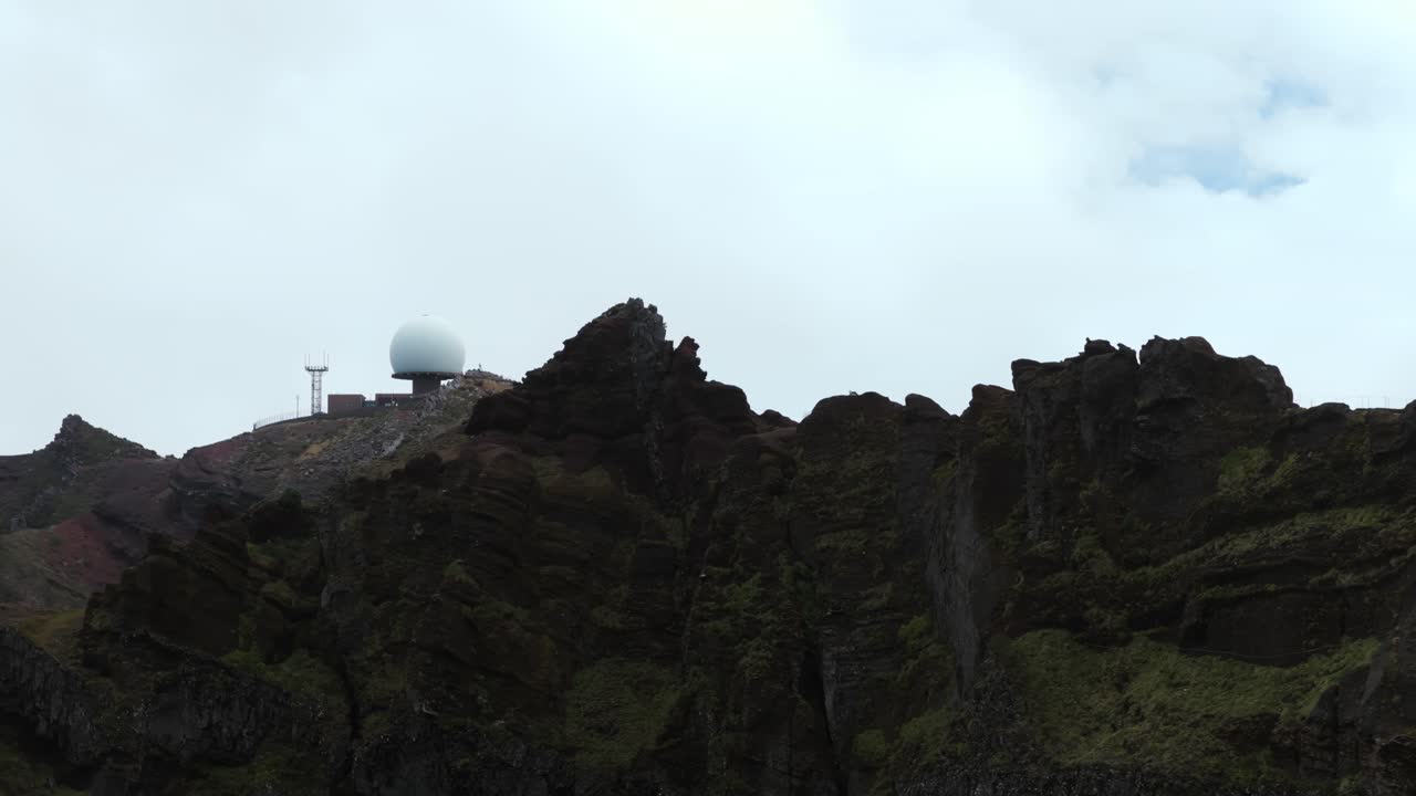 Aerial drone view of radar station on summit of Pico do Arieiro, rugged volcanic mountain peak under overcast sky, Madeira, Portugal