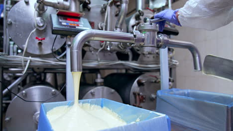 liquid butter pouring into a large box. use of spatula to flatten the dairy product in the container. factory worker holding his hand at the faucet to stop the flow of butter.