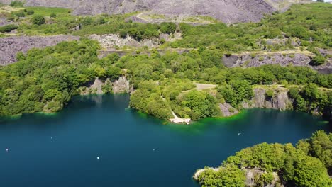 Aerial-view-Dorothea-slate-mining-quarry-woodland-in-Snowdonia-valley-with-gorgeous-transparent-blue-lake