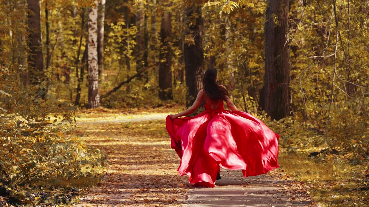 A Graceful Journey Through Autumn: A Woman in a Flowing Red Dress Captures the Essence of Nature's Beauty While Twirling Along a Leaf-Covered Path