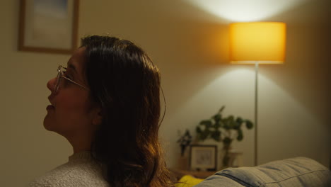 rear view of young woman sitting on sofa alone at home having conversation with person off camera