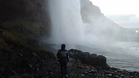 girl standing under waterfall slowmotion shot from bottom to top in iceland dark cave