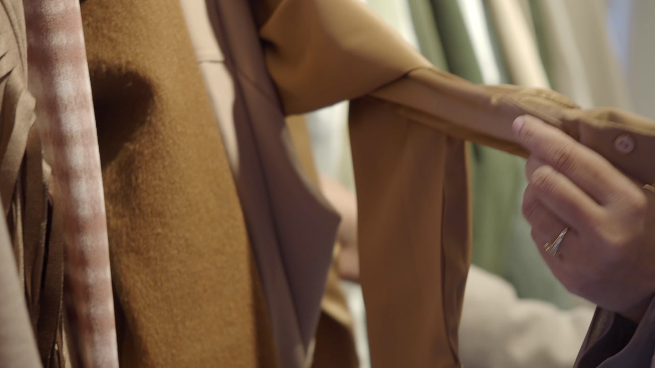 Close-up of Hands Examining Fabric on a Clothing Rack