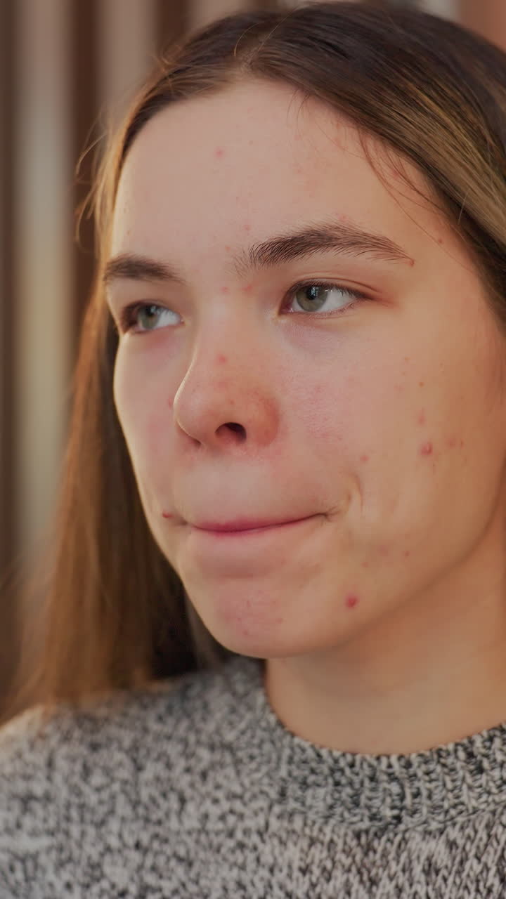 Primer plano del rostro de una joven caucásica dando un sorbo pensativo con una taza color menta, con una suave lámpara de fondo, textura de la piel visible con pecas y acné, expresión que pasa de pensativa a ligeramente