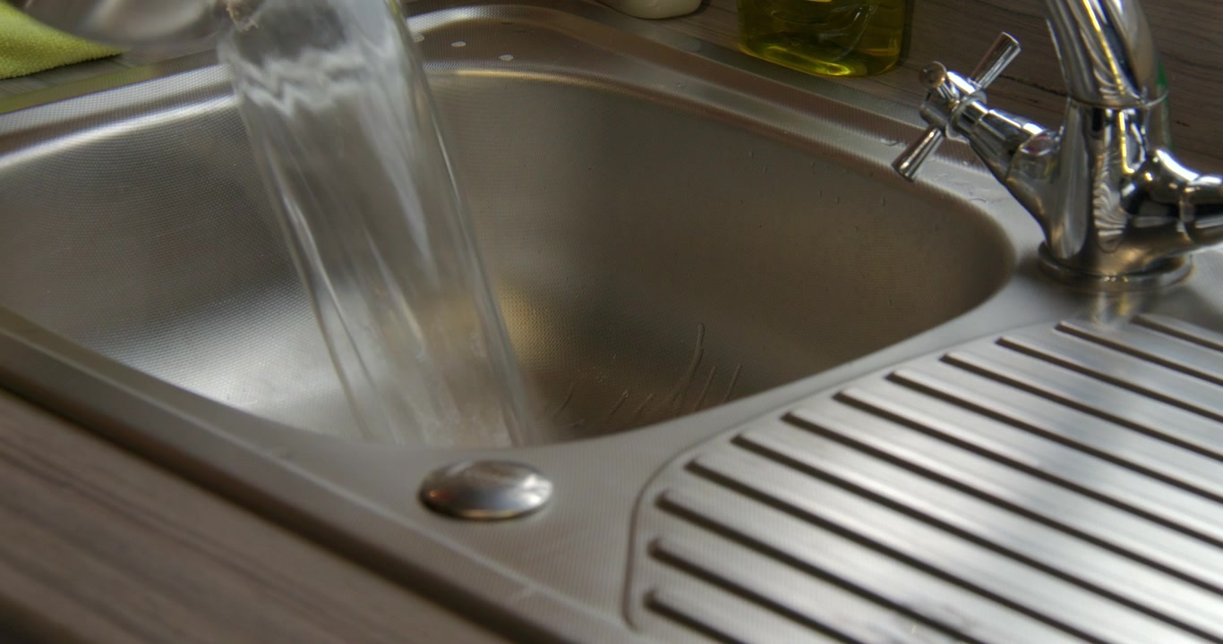 Toma de una olla con agua hirviendo vertiéndose en un fregadero de metal