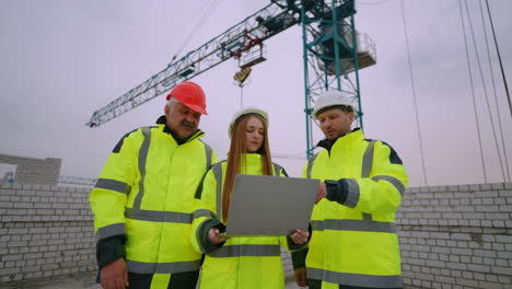 equipo de arquitecto ingeniero civil y capataz en el sitio de construcción mujer está sosteniendo una computadora portátil con el plan de construcción