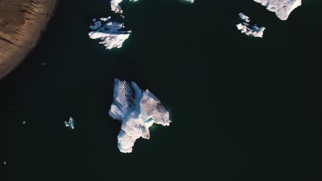 aerial view of glacial ice floating in dark waters with shadows casting on the icy surface