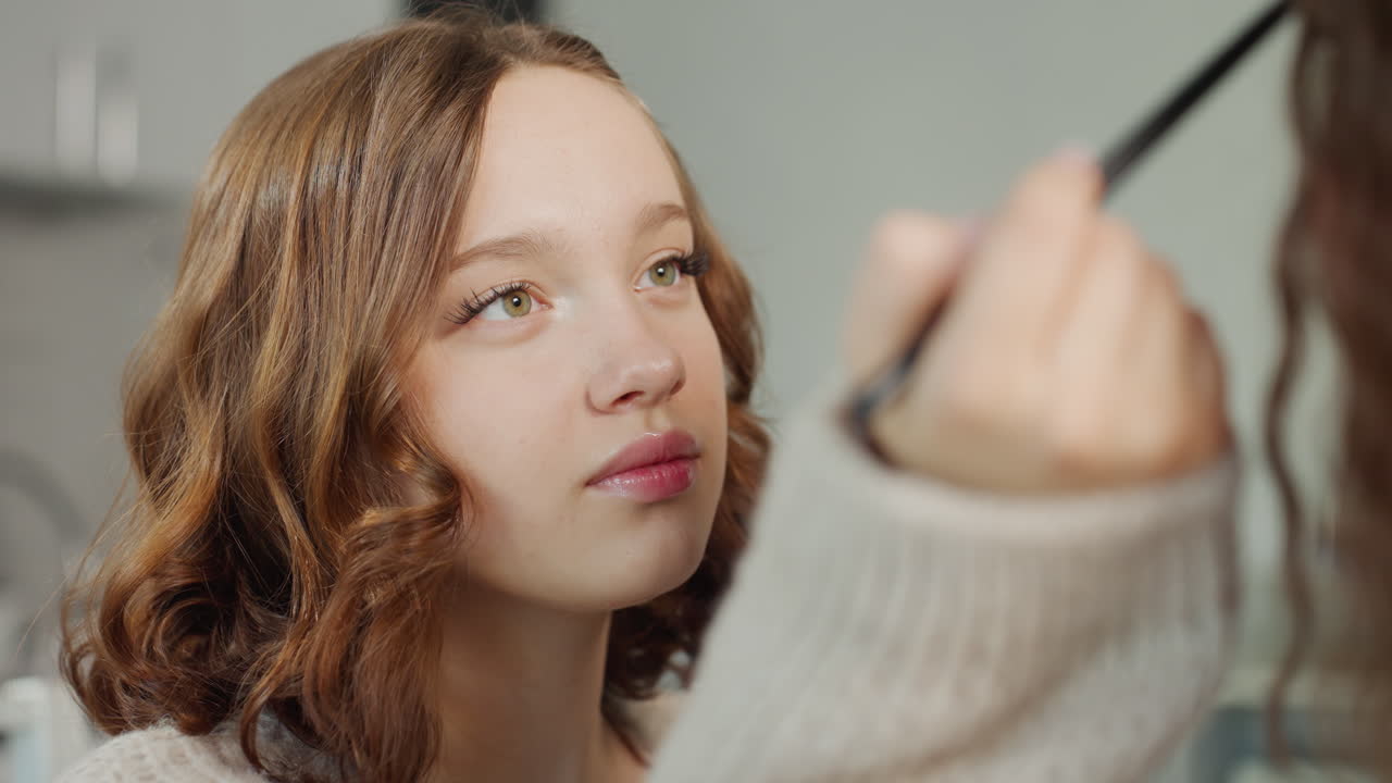 CloseUp Instructional Scene With Makeup Brush Near Eyes, Attentive Student Watches As Instructor Demonstrates Precise Strokes, Cozy Kitchen Lighting, Warm Teaching Vibe And Careful Cosmetic Technique