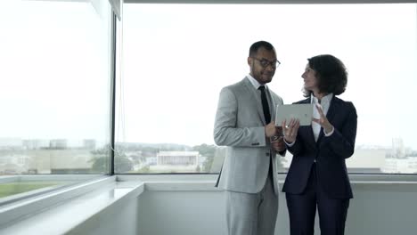 Smiling-people-wearing-formal-wear-using-tablet-near-window