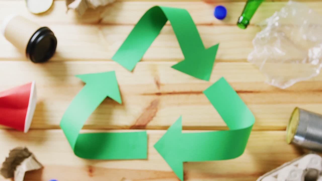 Close up of trash and recycling symbol of green paper arrows on wooden background