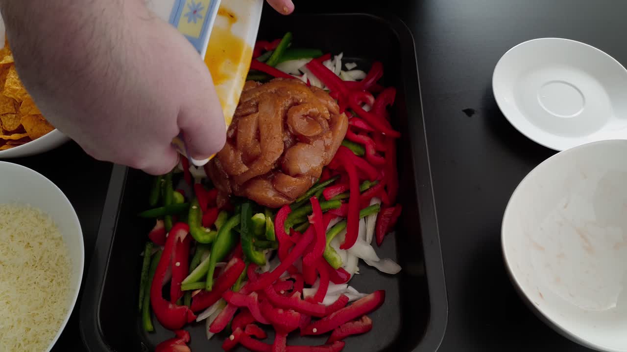 poner rebanadas de filete de pechuga de pollo sazonado en una bandeja para hornear con cebollas y pimientos cortados en juliana