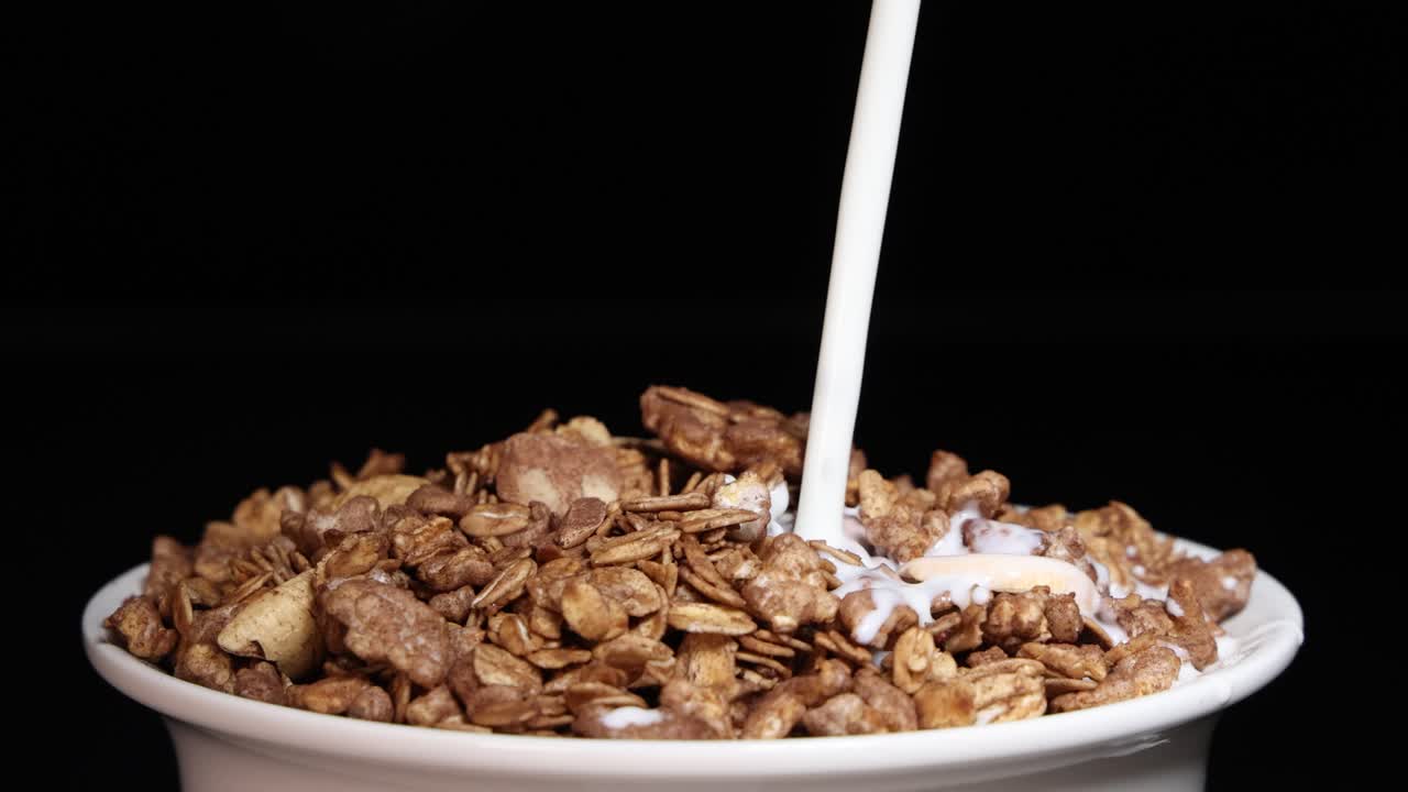 Milk cascades into a bowl of cereal, creating a dynamic splash effect against a dark background