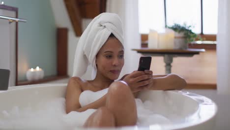 Mixed-race-woman-taking-a-bath-and-using-smartphone