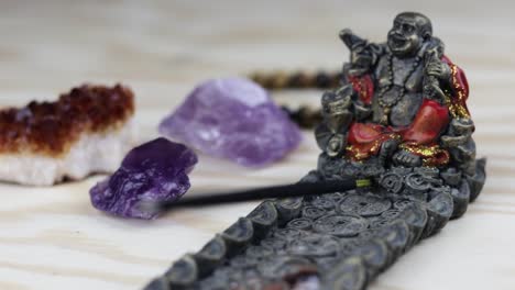 a stick of incense burning on a buddha holder, with crystals in the background