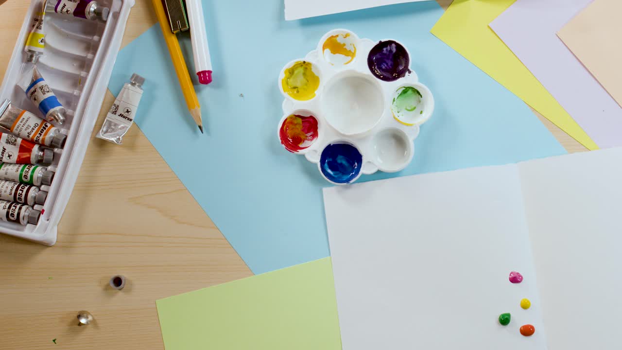 Overhead shot of hands applying paint to paper on a desk with art materials