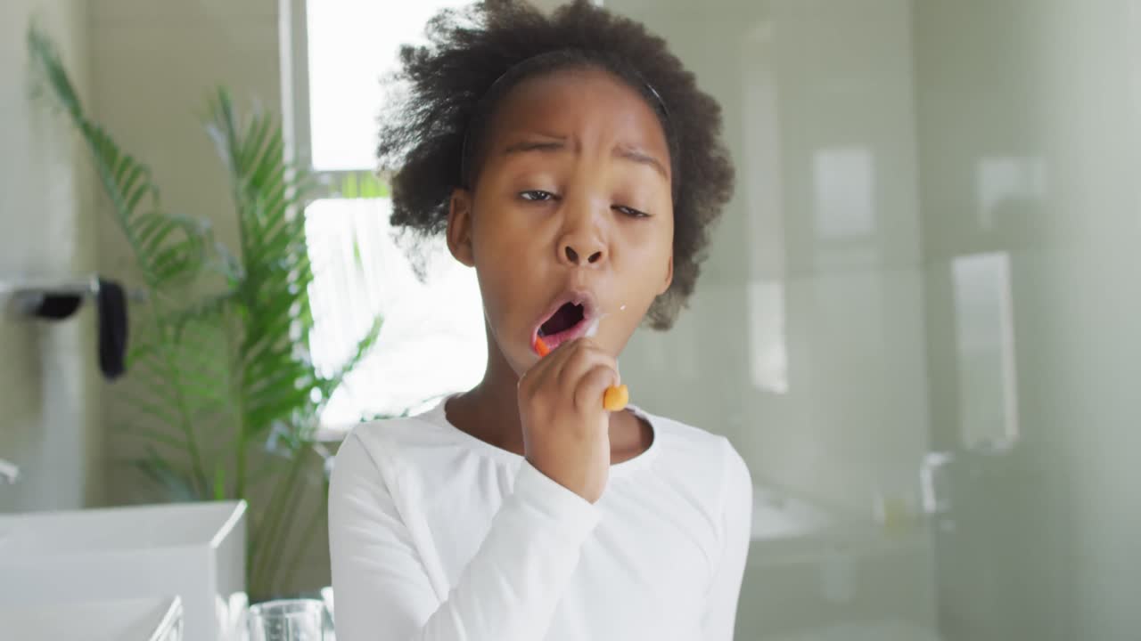 Video of african american girl brushing teeth in bathroom