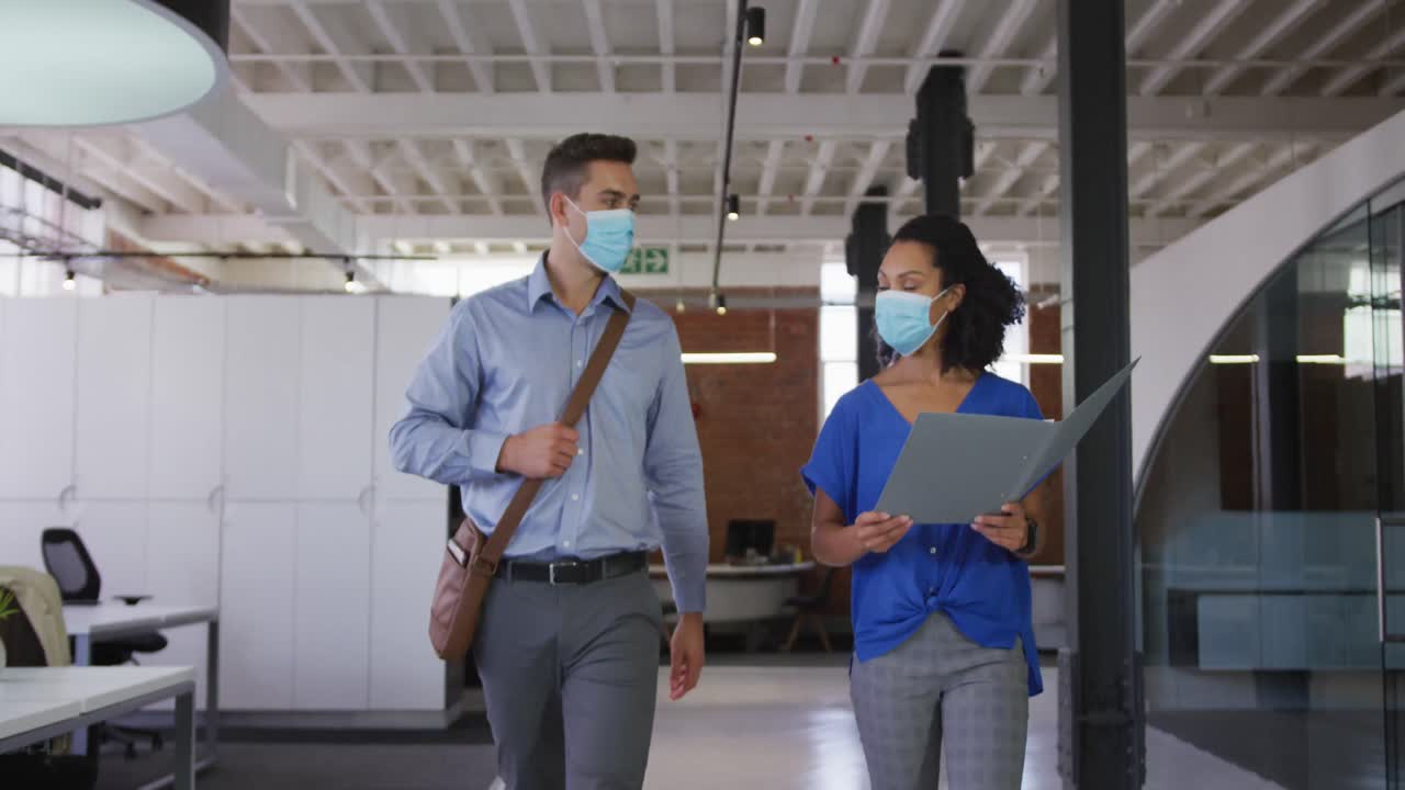 Diverse race male and female businessmen walking discussing through corridor wearing facemask