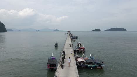 aerial follows woman walking by boats at floating pier in tropical sea