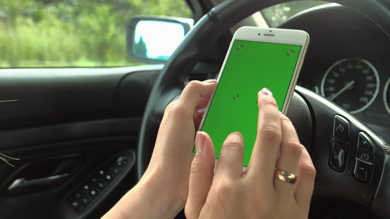 las manos de las mujeres sostienen un teléfono con una pantalla verde con las manos en el volante del coche. la chica conductor está sentada al volante sosteniendo un teléfono con un llave de croma en las manos