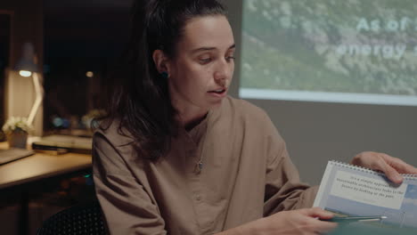 young female engineer holding paper slides and giving presentation about green energy project to team, working together on startup during night office meeting