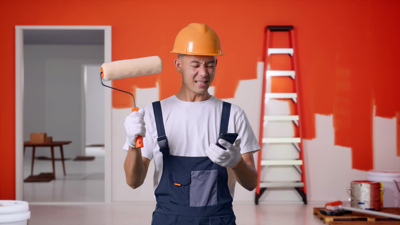 Asian Man Painter Wearing Safety Helmet Looking At Smartphone Then Screaming Goal Celebrating While Standing With Painting Wall In Room