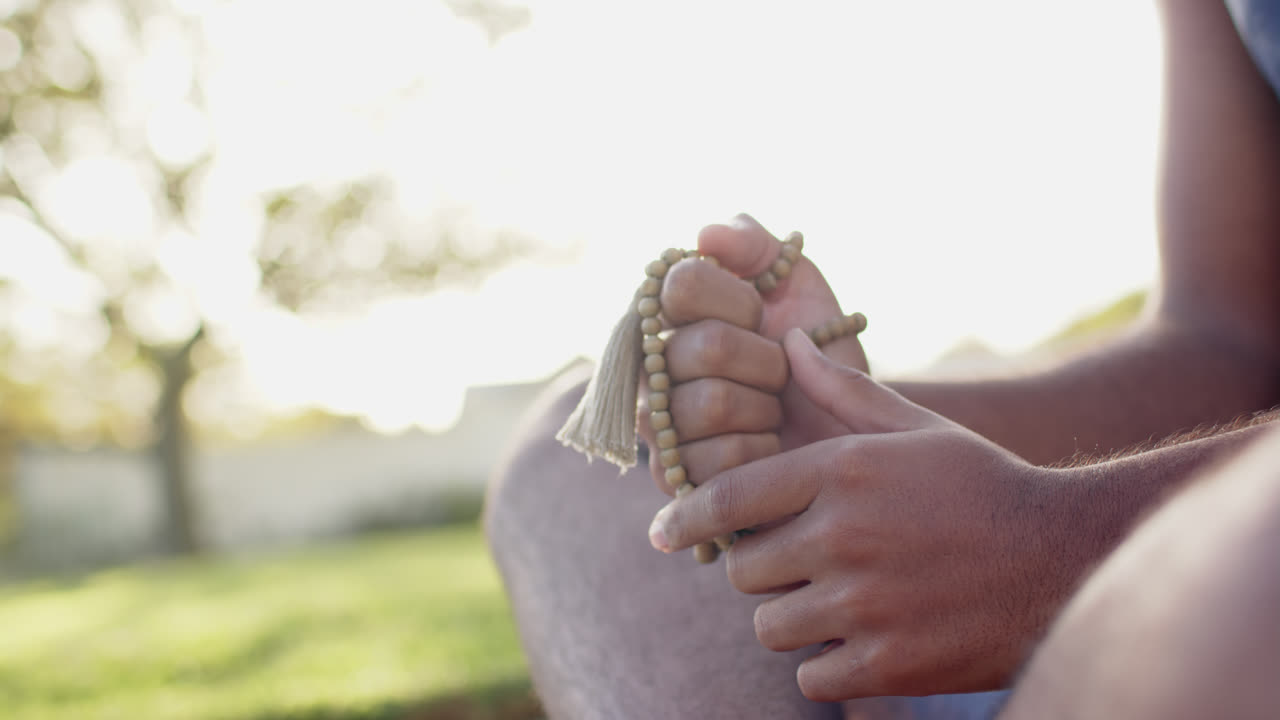 sección media de un hombre biracial practicando meditación de yoga en un jardín soleado, cámara lenta