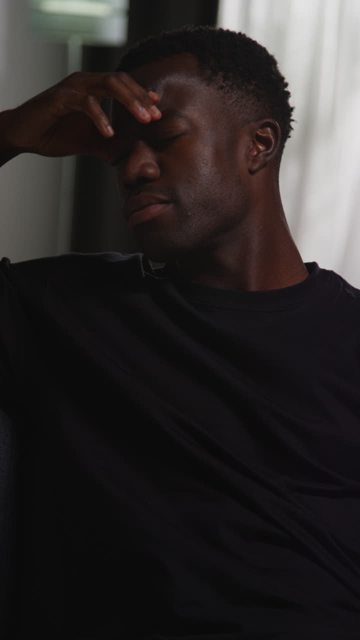 Vertical Video Of Unhappy And Depressed Young Man Sitting On Sofa At Home Looking Anxious And Worried Resting Head On Hand 9