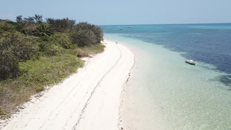 drone aerial going backwards over white sandy beach and boat of clear blue water