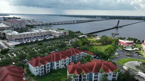 aerial flyover bradenton, florida, showing red-roof residential complexes, waterfront buildings and long bridge spanning across the bay under cloudy day