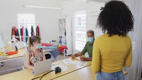 diseñadores de moda con máscaras hablando entre sí en el estudio