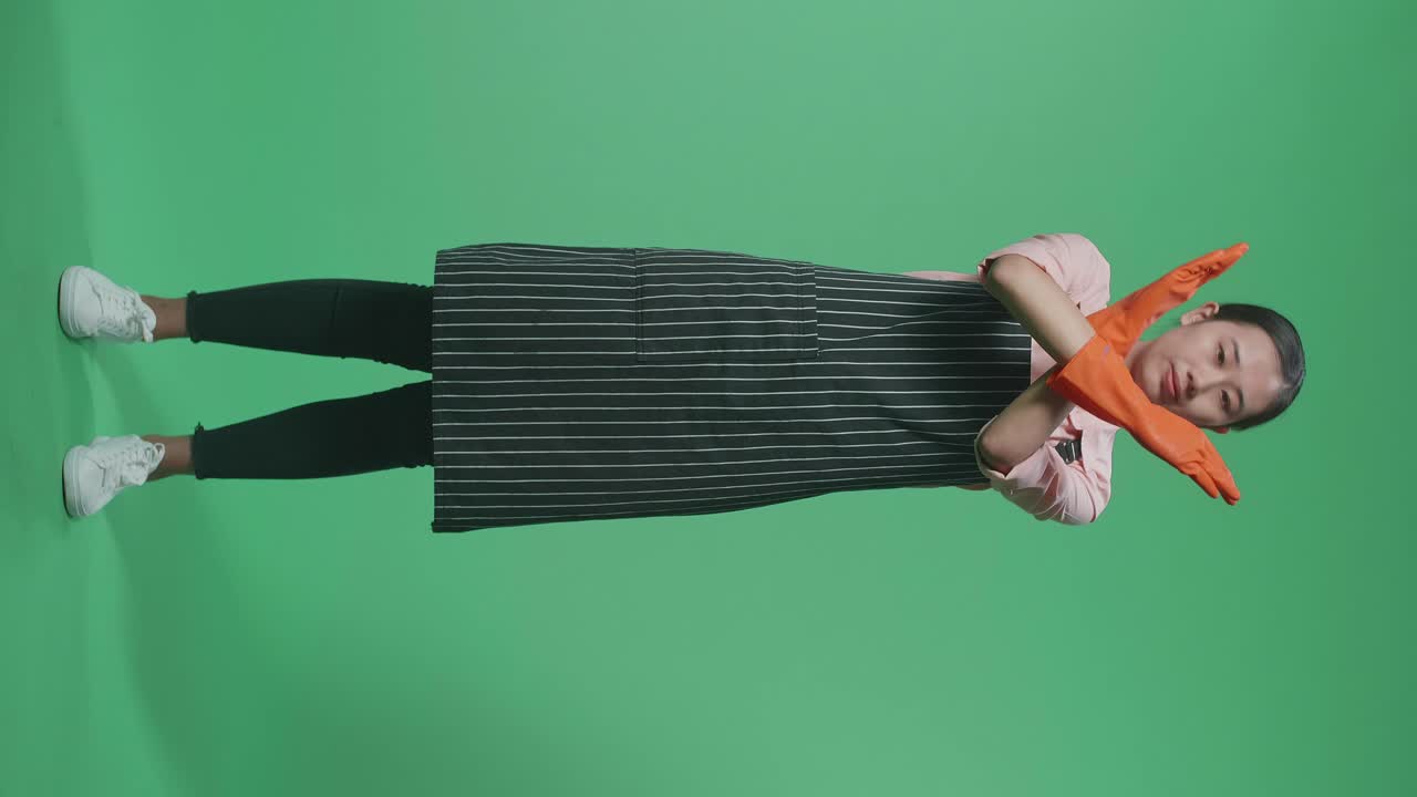 녹색 스크린 스튜디오에 서 있는 동안 금지 행동을 보여주는 전면으로 동의하지 않는 아시아 여성 집주인이 가득 차 있습니다.