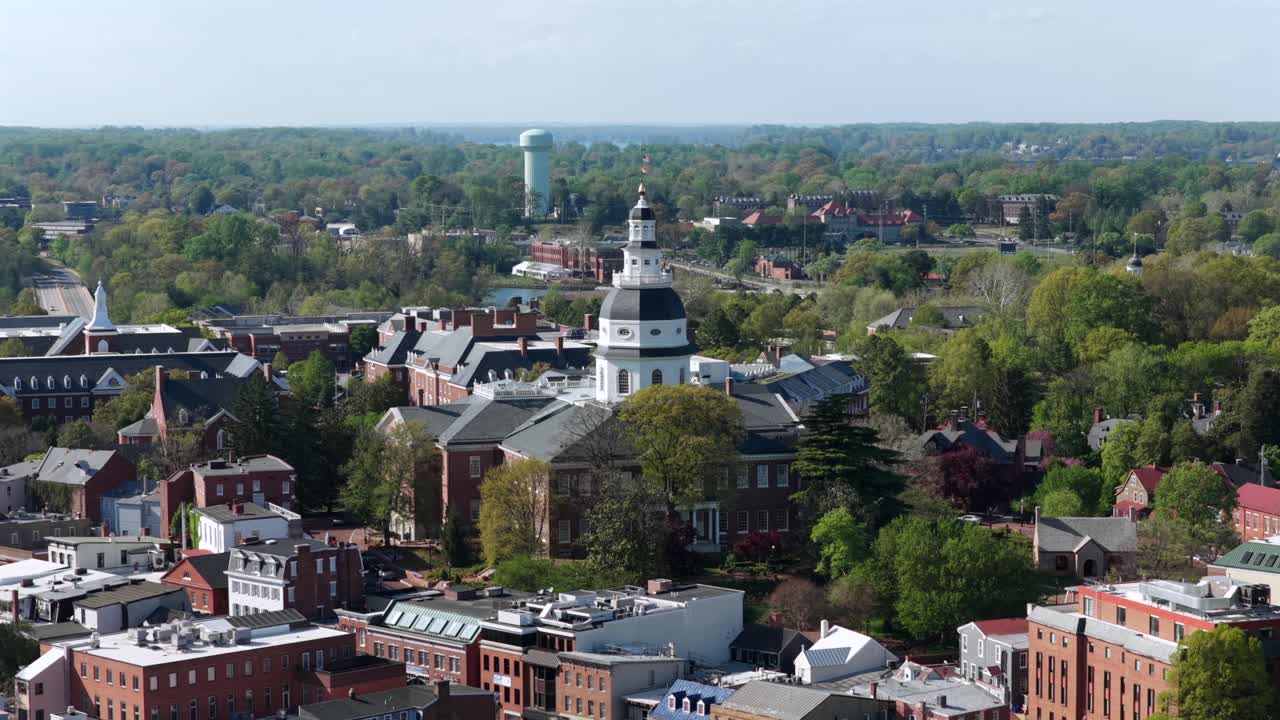 Etablerende luftfoto av Annapolis, Maryland, USA, med State House-kuppelen og vanntårnet som rager over historiske bygninger og frodige vårtrær under sterkt sollys i det naturskjønne hovedstadsområdet.